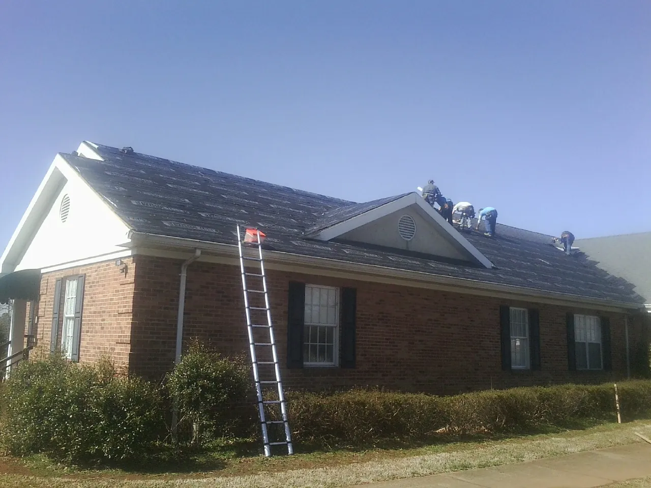 Crew tearing shingles off a brick ranch roof with a ladder set — Metal Roof Repair work by our crew in Warden