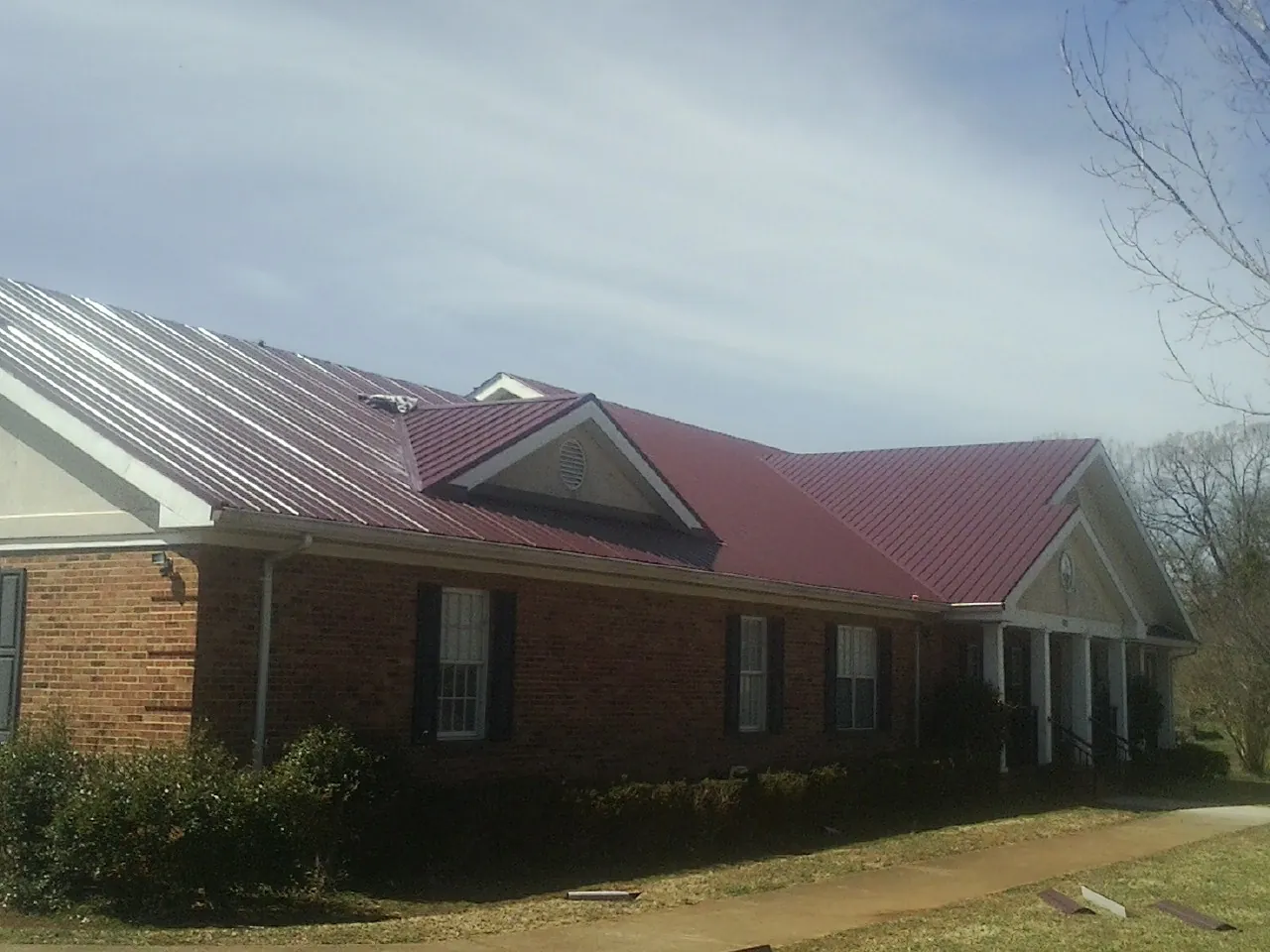Red metal roof with gabled entries on a long brick building, from a Hail Damage Roof Repair job in Warden