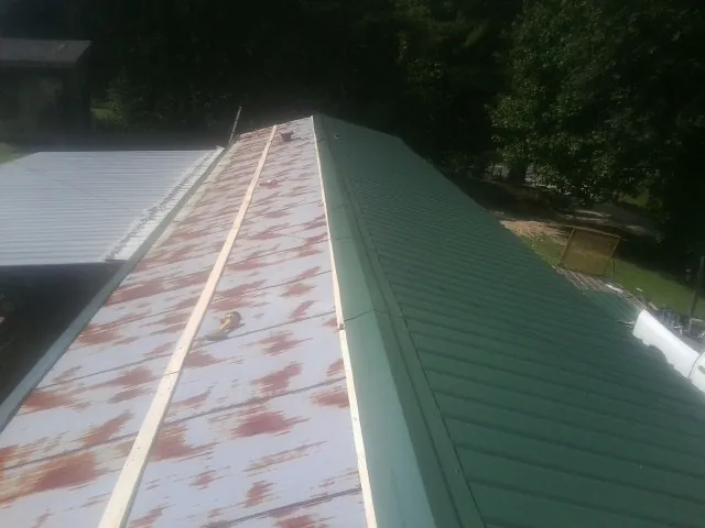 Old rusted panels beside newly installed green metal roofing — Wind Damage Roof Repair by Roofing Brothers in Warden