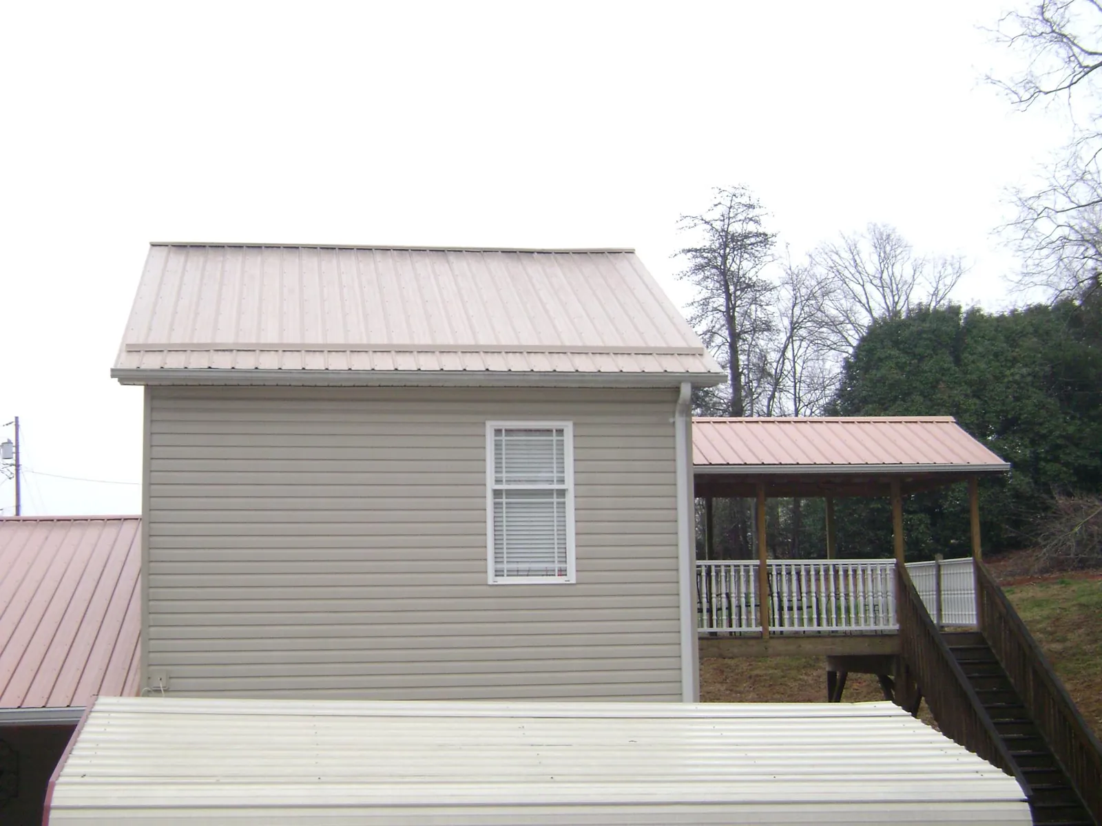 Tan metal roofs on a two story addition and attached porch, from a Roof Replacement job in Warden