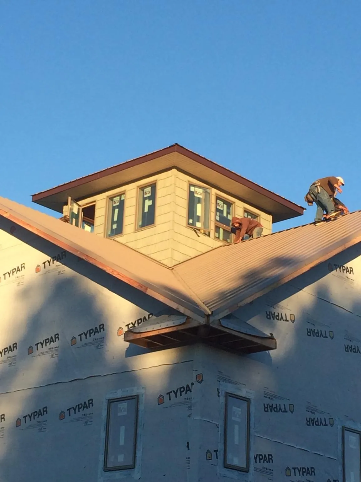 Roofers working around a rooftop cupola on a new metal roof at sunset — Roof Waterproofing in Warden by Roofing Brothers